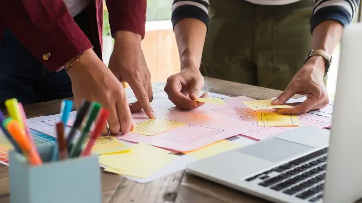 Two people organizing sticky notes on a desk